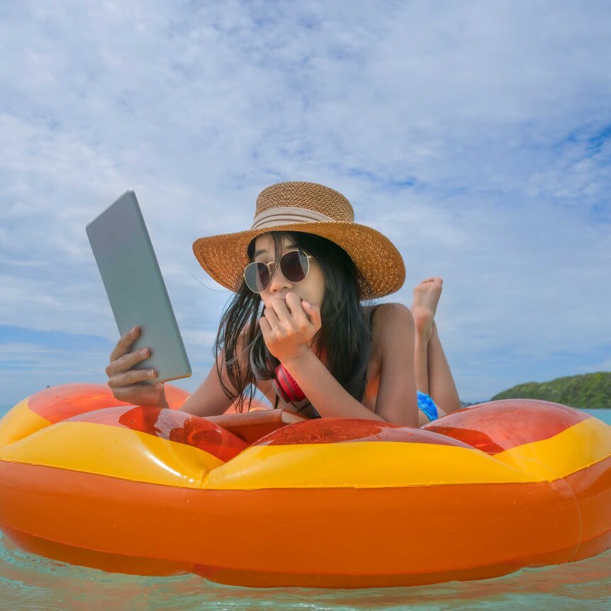 A woman reads from an ebook on an orange float.