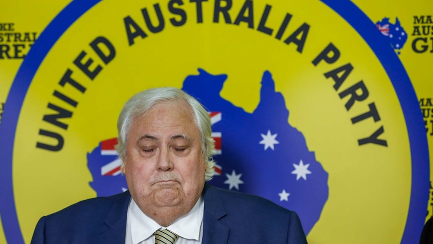 Clive Palmer frowns behind a yellow sign that reads United Australia Party.