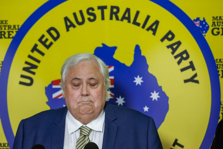 Clive Palmer frowns behind a yellow sign that reads United Australia Party.