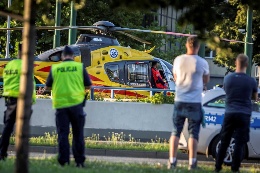 A helicopter stands with its front door open at a cycling race, with Polish police in foreground.