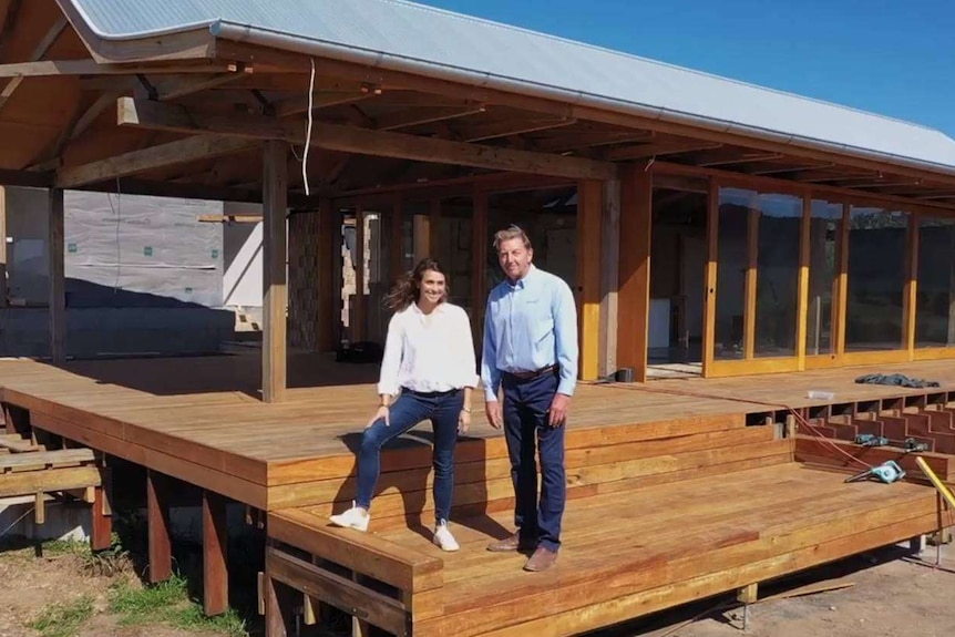 A man and a woman stand out the front of a half-completed house.