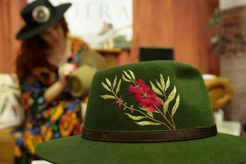 Green emroidered hat with beautiful Australiana bottlebrush design, Jules in background embroidering.