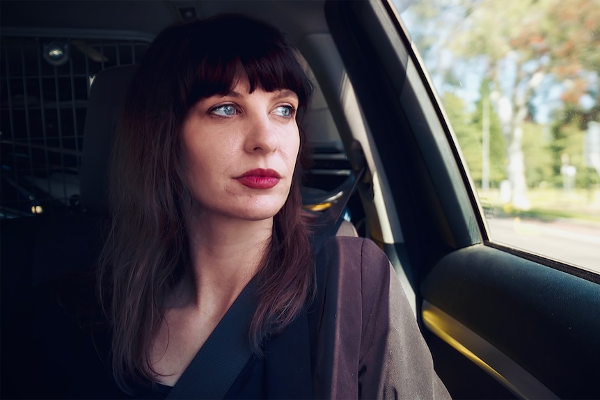 A woman looks out the window from the backseat of a car.