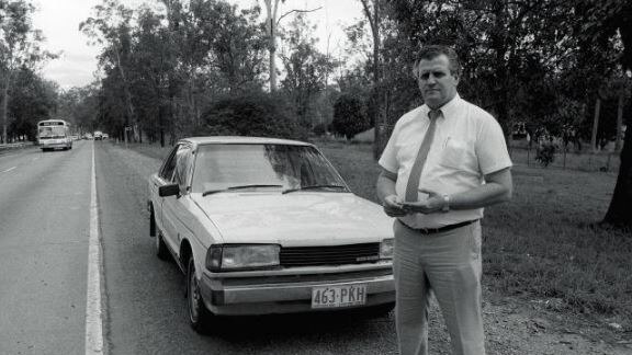 Black and white photo of man standing next to car