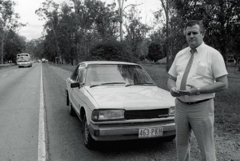 Black and white photo of man standing next to car