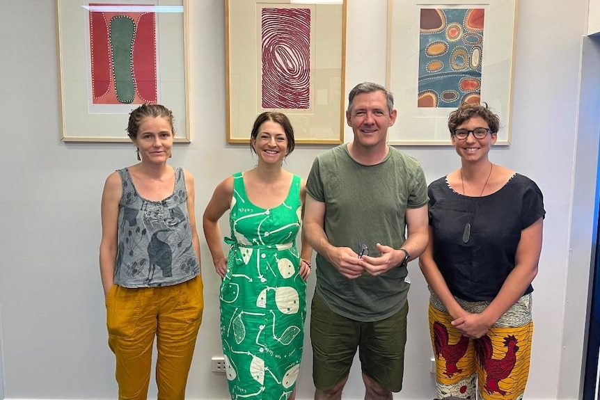 Three women and a man in a room with aboriginal art. Casually dressed.