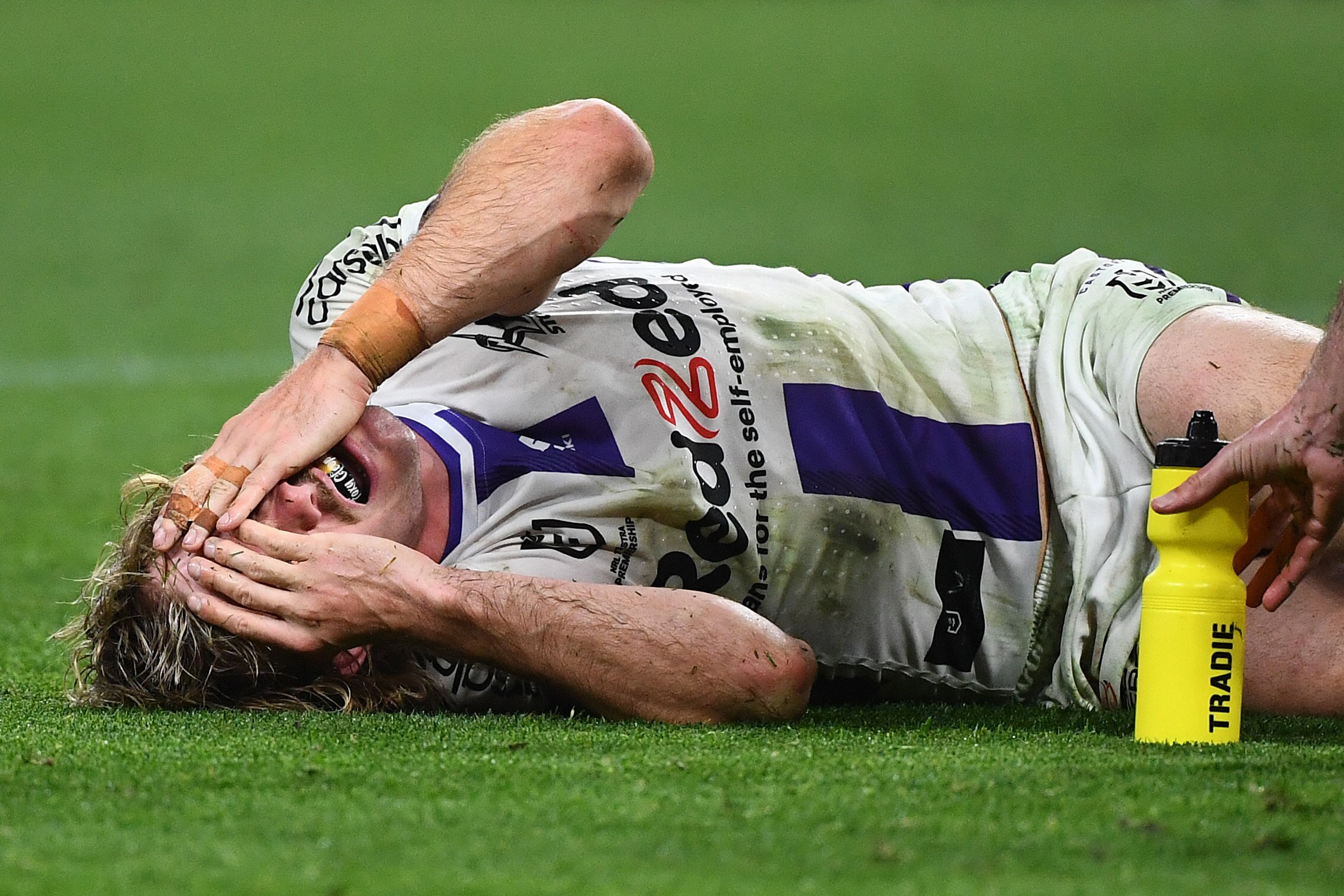 A Melbourne Storm NRL player lies in agony holding his face after sustaining a leg injury.