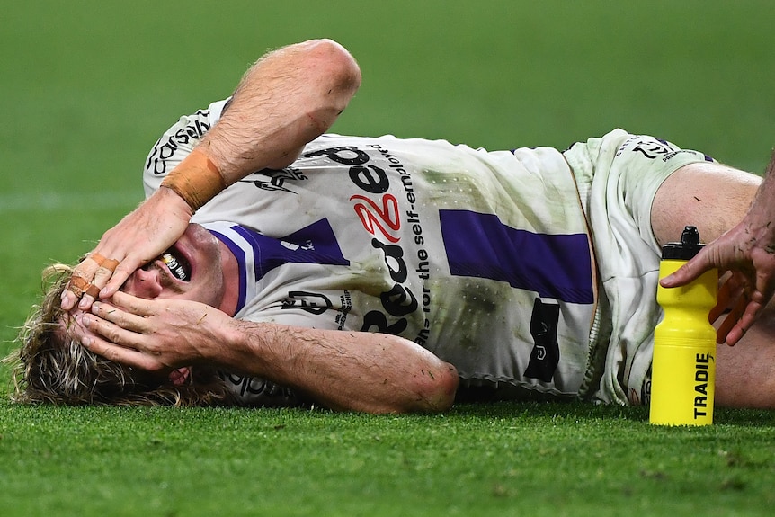A Melbourne Storm NRL player lies in agony holding his face after sustaining a leg injury.