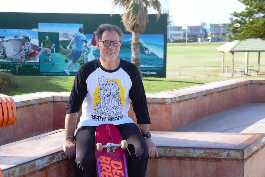 A man wearing glasses sits on a concrete bench with his skateboard. 