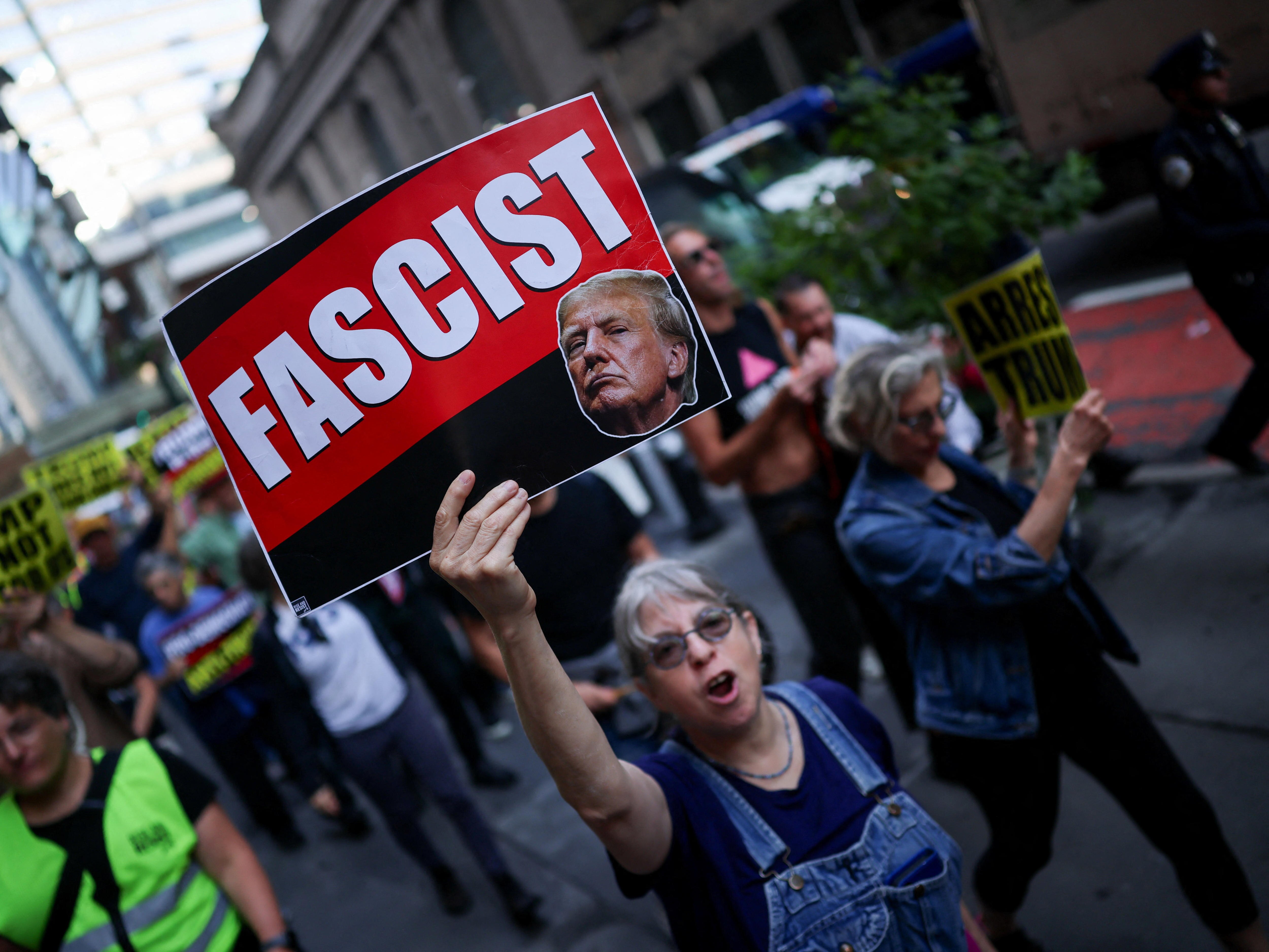 A woman holds a placard with the word 'fascist' and Donald Trump's face.