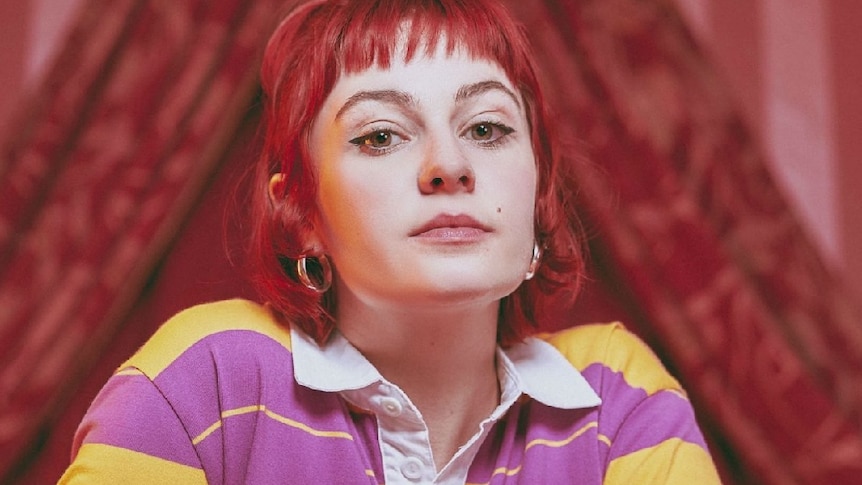 Biig Piig (aka Jess Smyth), with red hair and wearing a yellow and purple striped top