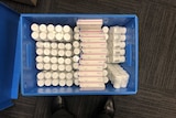 Boxes of medications and bottles of tablets wrapped in plastic in a blue box.