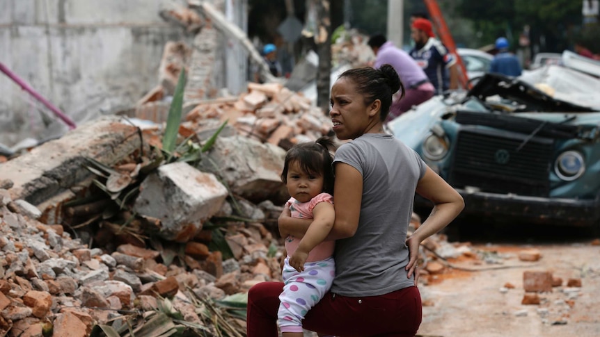 A woman holds her child as she stands next to wall turned to rubble when it collapsed during a massive earthquake