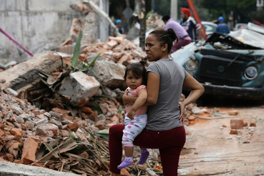 A woman holds her child as she stands next to a wall that collapsed during the massive earthquake.