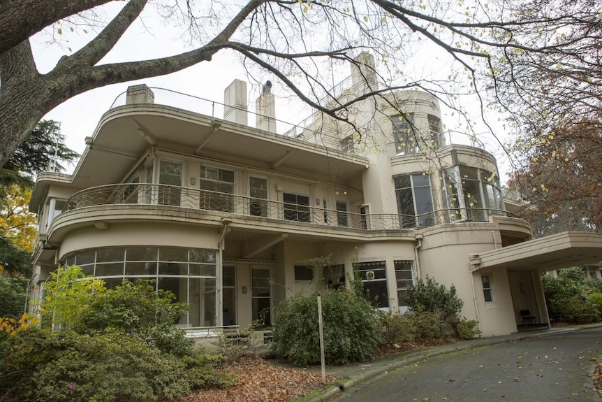 A white Art Deco mansion with lots of curves, surrounded by trees.