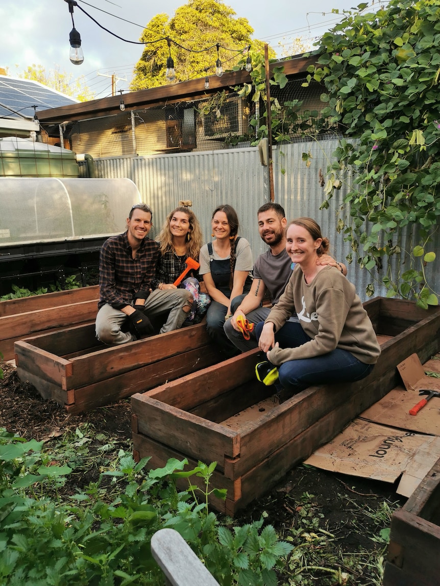 Koren Helbig sits on the edge of a raised garden bed with four friends who helped her construct them in her garden.