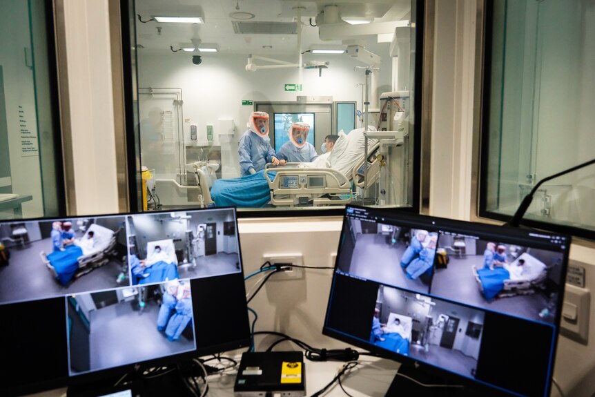 camera footage on a computer monitor with patients, nurses and doctor in hazmat suits in background
