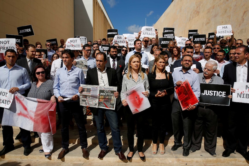 A large group of people stand holding protest signs.