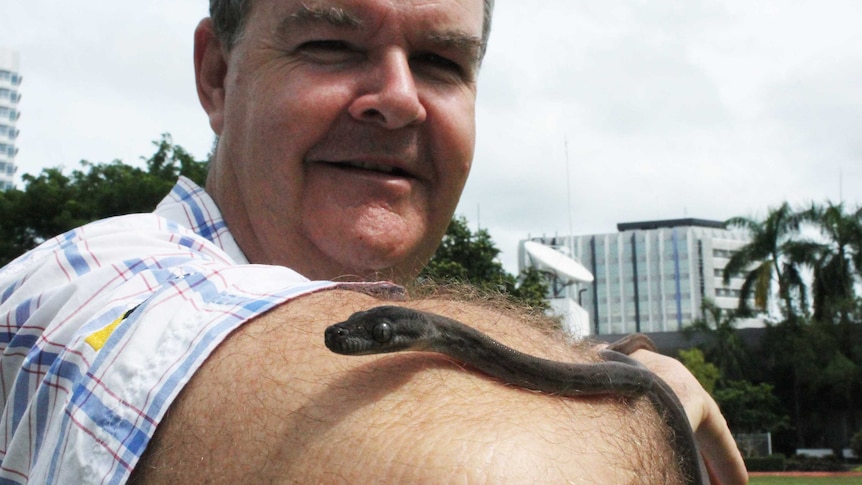 A middle-aged man with a small python on his hand.