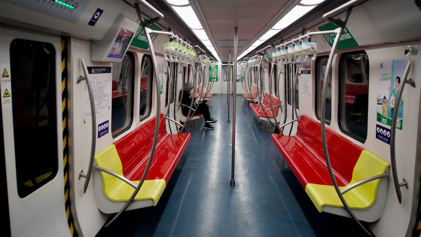 A single passenger sits on an otherwise empty subway train.