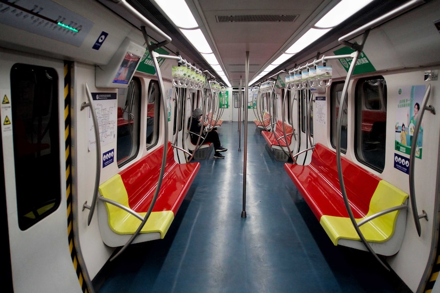 A single passenger sits on an otherwise empty subway train.