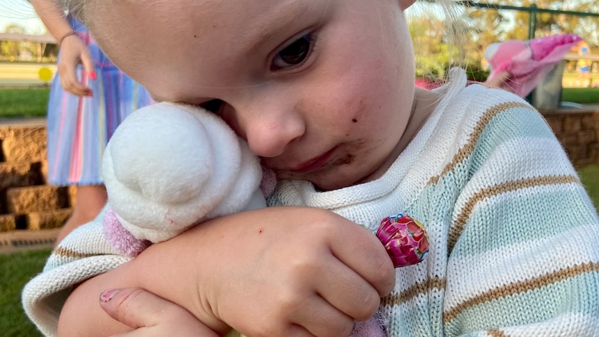 a little girl cuddles a stuffed toy and looks sad.