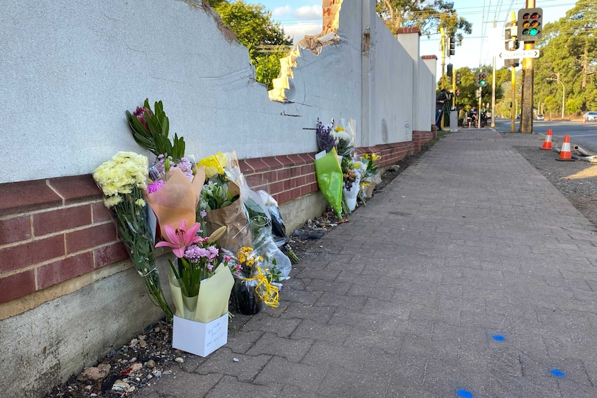 Bunches of flowers left laying against a white wall on a footpath