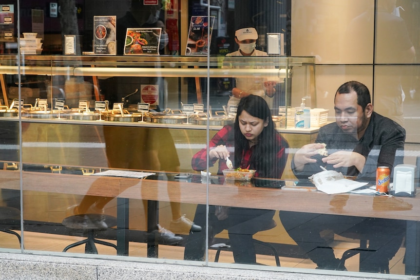 Two people sit inside a takeaway restaurant eating a meal