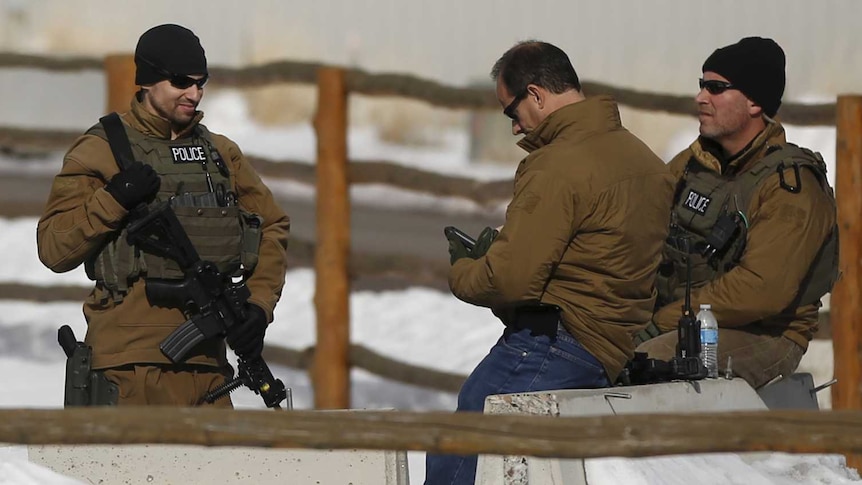 Members of FBI and Oregon State Troopers holding guns stand on snowy ground within a wooden fence