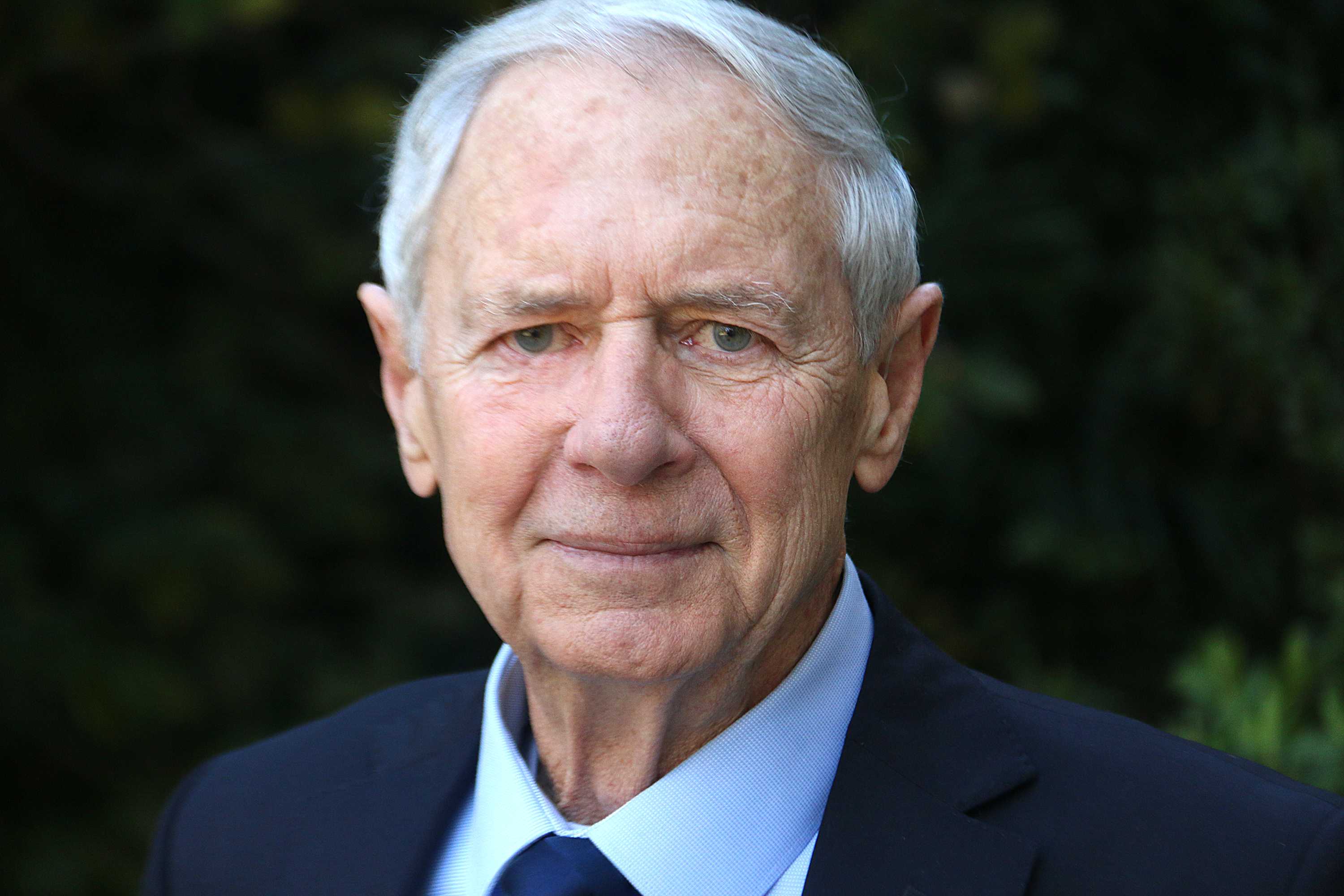 A headshot of a white-haired man in a suit.
