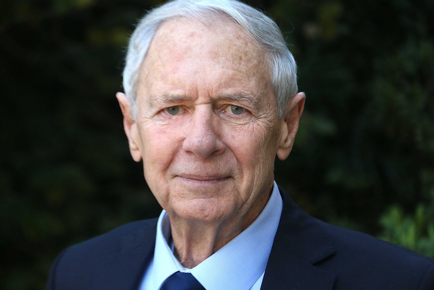 A headshot of a white-haired man in a suit.