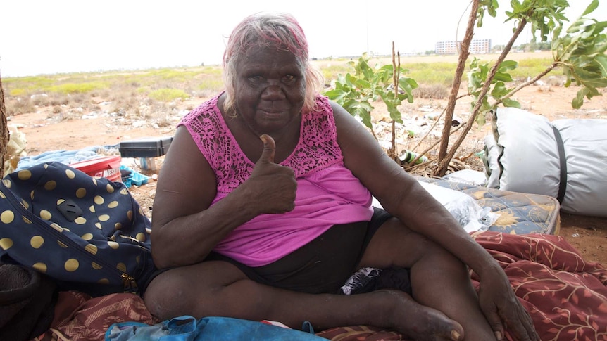 An Aboriginal woman sits on a sheet in scrub on the edge of Hedland