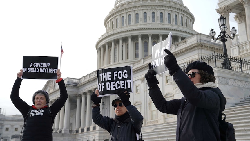 Three female protesters wearing black standing outside the US Capitol building with placards