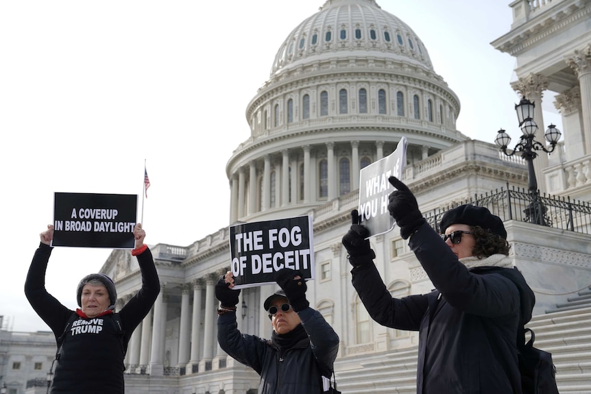 Three female protesters wearing black standing outside the US Capitol building with placards
