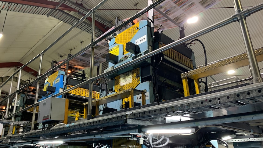 Papers run on a conveyor belt on a complicated machine in a warehouse.