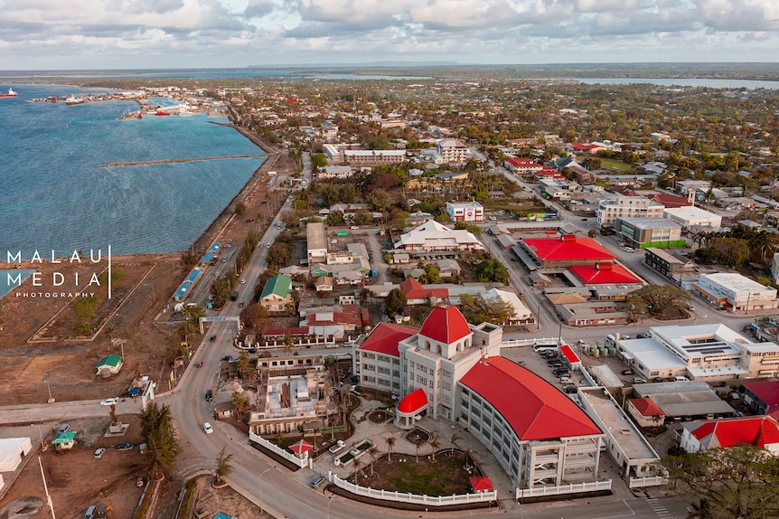 Aerial image over Tonga, Large building red roof surrounded by homes and structures. 