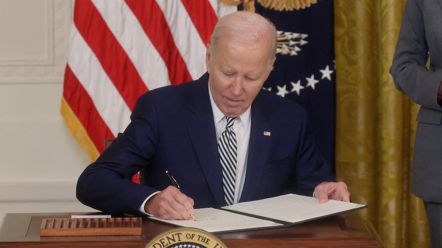 Joe Biden signing a bill in front of the US flag.
