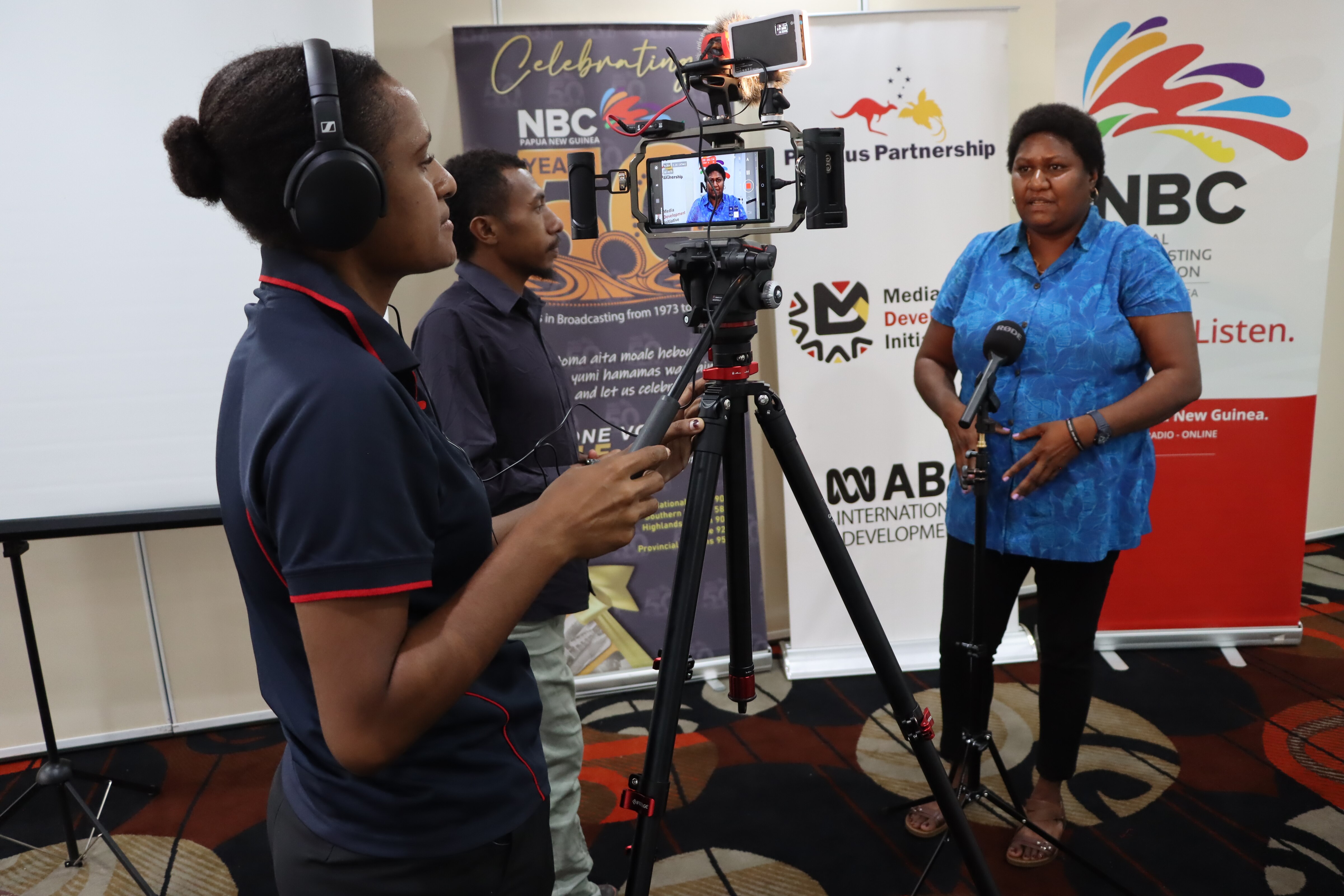Three journalists operating a tripod with a mobile phone and microphone