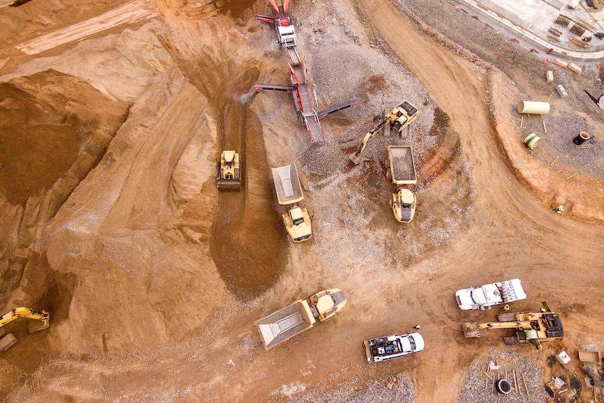 Bird's eye photograph of a sandy mining setting with trucks and conveyors.