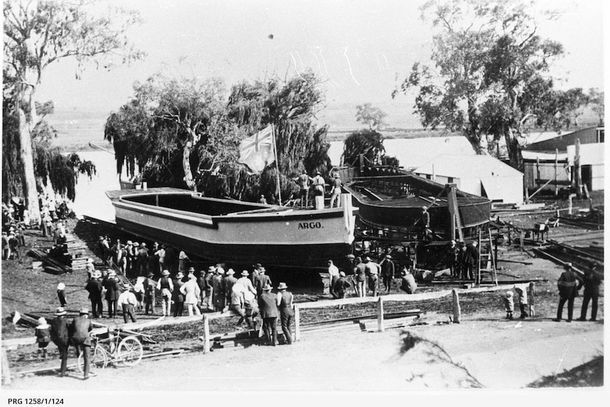 A black and white photo of a barge that says Argo being launched into the river with lots of people around.