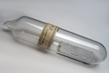 A glass vial with a thin sheet of metal inside and a hand-written label reading 'Thorium'
