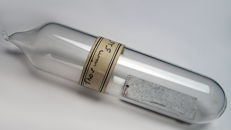 A glass vial with a thin sheet of metal inside and a hand-written label reading 'Thorium'