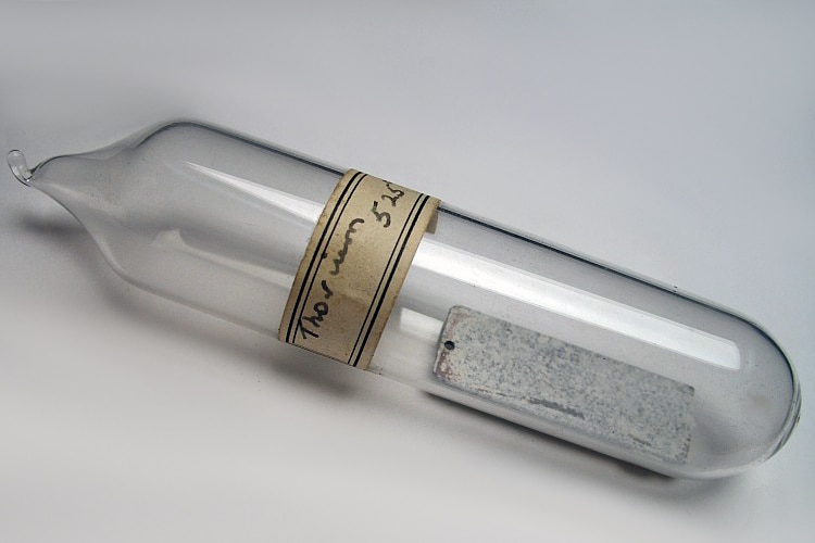 A glass vial with a thin metal plate inside and a handwritten label that says 