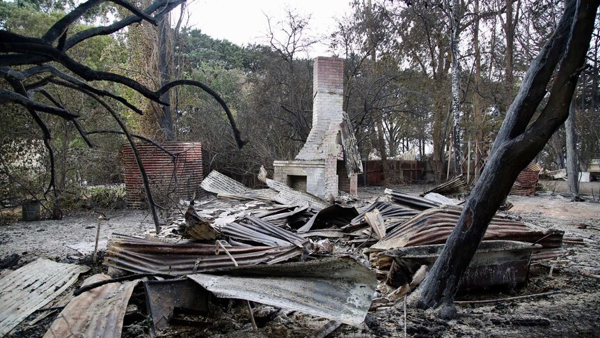 A brick chimney stands behind the flattened remnants of a burnt-out building.
