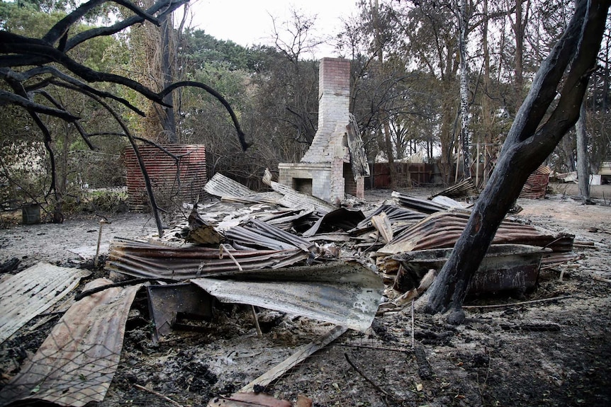 A brick chimney stands behind the flattened remnants of a burnt-out building.