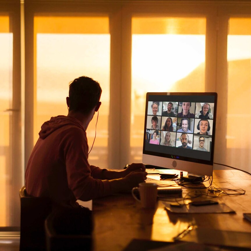 Man sitting at laptop on video conference call screen filled with faces and he looks out his window.