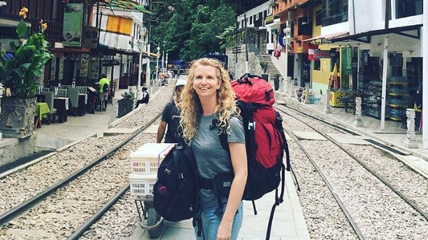 Woman standing on railway line in Peru, South America, wearing backpack.