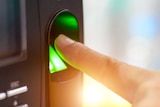 Close-up shot of a finger hovering over the green glowing light of a small black machine with a screen and buttons.