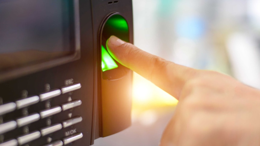 Close-up shot of a finger hovering over the green glowing light of a small black machine with a screen and buttons.