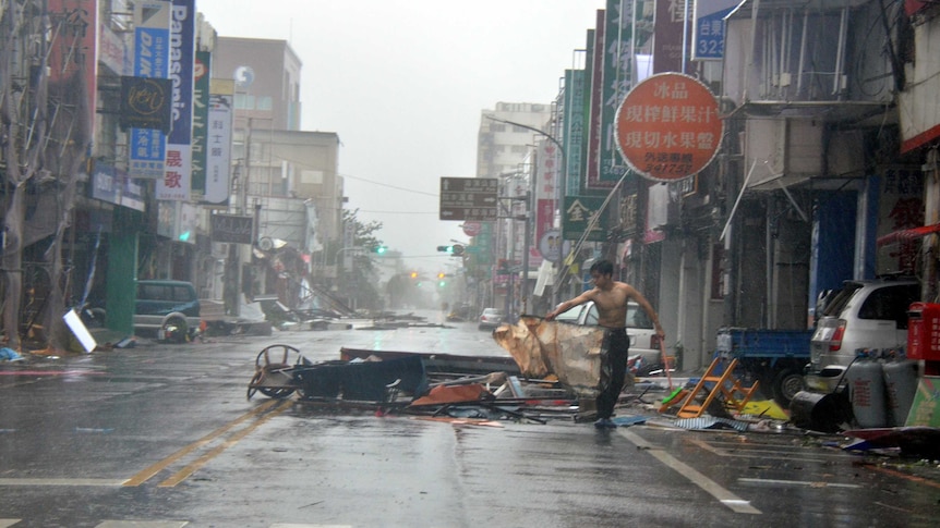 A man is holding onto debris in front of a row of shop fronts.